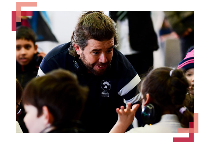 A picture of a man with a Bristol Bears jersey speaking to children